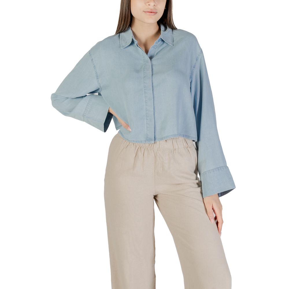 Woman wearing Only Light Blue Lyocell Blouse with long sleeves and cropped design, paired with beige trousers.