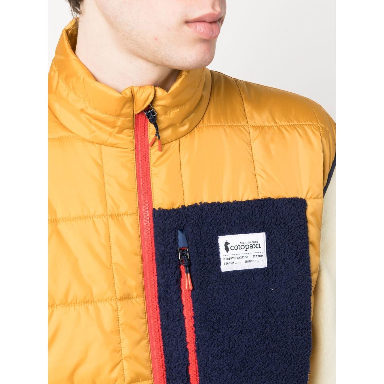 COTOPAXI yellow padded gilet with chest logo patch, front zip fastening, and sleeveless design. Model wearing size M.