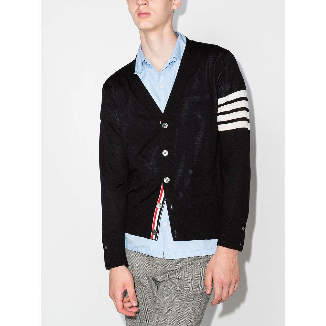Model wearing a Thom Browne Sweaters Blue navy wool cardigan with 4-Bar stripe and RWB detail, showcasing button fastening and side slits.