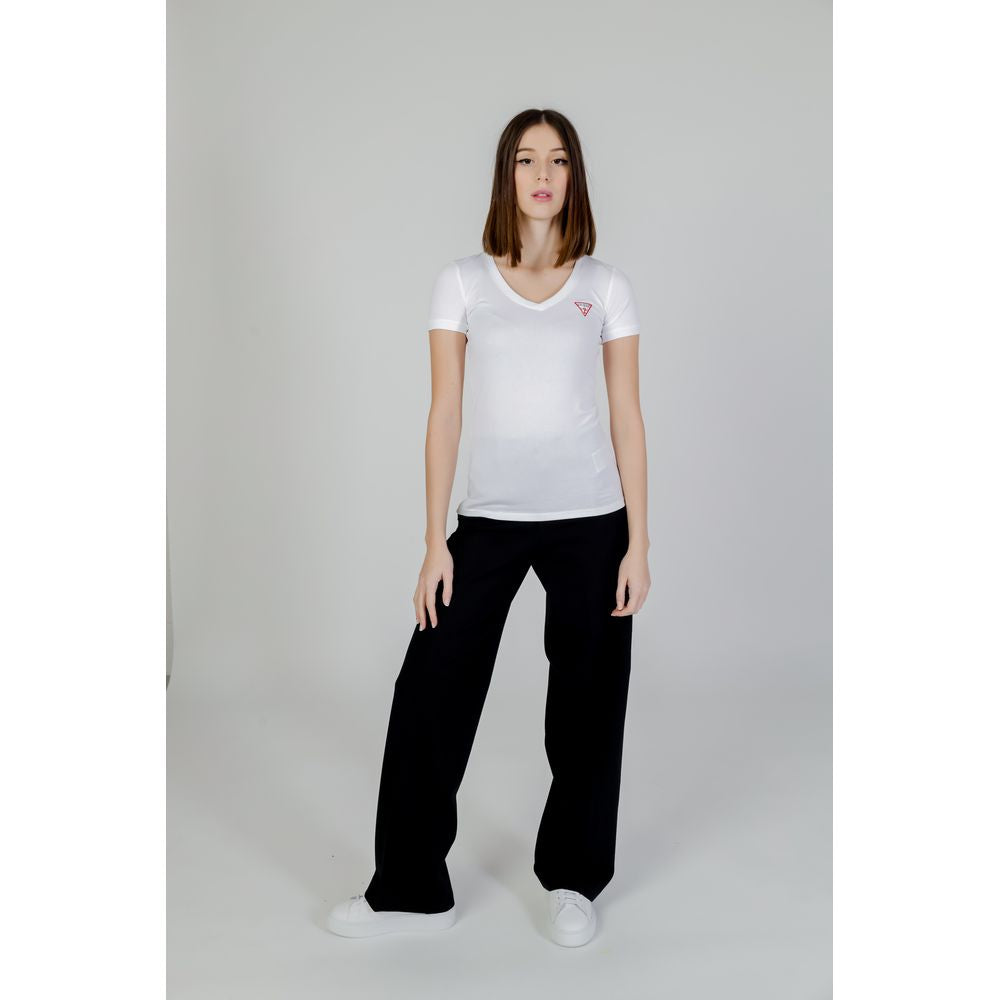 Woman wearing Guess White Cotton T-Shirt with mini triangle logo, short sleeves, and V-neckline, styled with black pants in a minimalist setting.