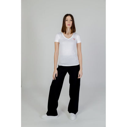 Woman wearing Guess White Cotton T-Shirt with mini triangle logo, short sleeves, and V-neckline, styled with black pants in a minimalist setting.