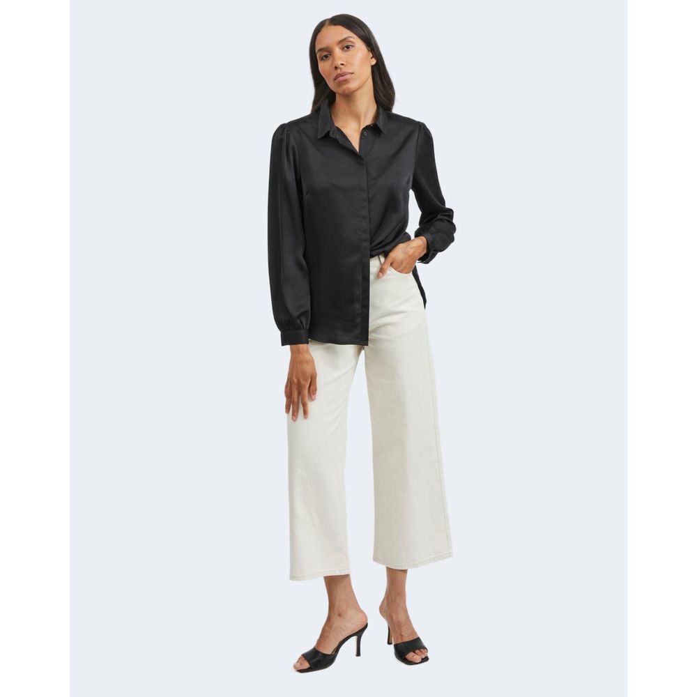 Woman wearing Vila Clothes Black Polyester Blouse with white pants and heels, showcasing a long-sleeve satin shirt for versatile styling.
